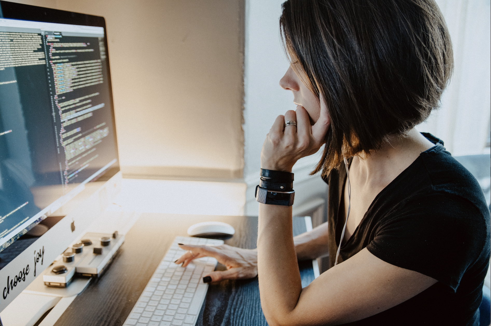 A woman sitting at her desk in front of a screen of coding, having just looked up 'What is Paddle.com?'